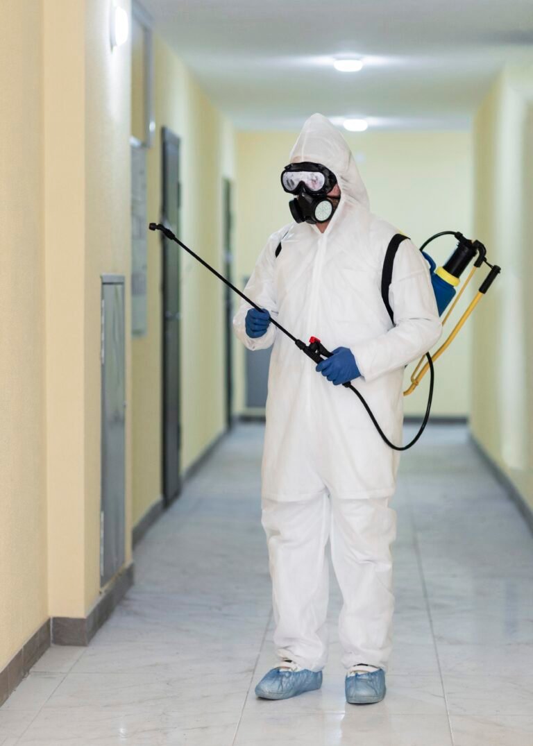 Pest control worker in full protective gear spraying chemicals in a hallway.